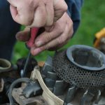 A mechanic uses a screwdriver to repair a lawn mower engine. His hands are dirty from oil coming from the machine.
